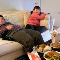 overweight brother and sister sitting on a sofa eating takeaway food and watching the tv - junk food stock pictures, royalty-free photos & images