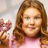 overweight girl (8-9) eating doughnut, smiling, portrait, close-up - junk food stock pictures, royalty-free photos & images