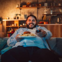 overweight man eating fast food and watching television - junk food stock pictures, royalty-free photos & images
