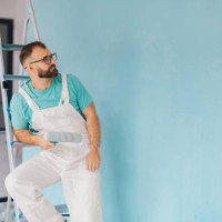 painter sits on ladder with roller by blue wall - home decoration stock pictures, royalty-free photos & images