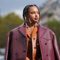 Paola Locatelli wears a necklace, an orange wool mini dress, a brown leather jacket, a burgundy leather texture oversized jacket, outside Miu Miu,...