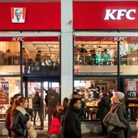 Pedestrians walk past the American fast food chicken restaurant chain, Kentucky Fried Chicken and its logo in Madrid.