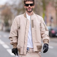 Pelayo Diaz wears black sunglasses, white sweater, light brown unzipped jacket, light brown shorts, black leather gloves, outside Sacai, during the...