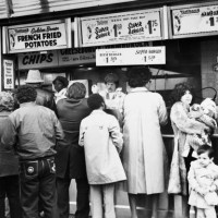 People wait to be served at Nathan's sidewalk food stand in Coney Island, in the borough of Brooklyn, New York City, New York, 1982. The menu lists...