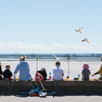 People with children sit on the seawall eating chips as various food businesses start to open for takeaway only along the promenade during the...