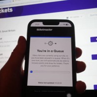 Person in a queue to access the Ticketmaster website on their phone, with the StubHub website in the background, detailing information about Oasis...
