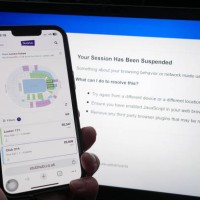 Person who has had their Ticketmaster session suspended on a laptop, as the StubHub website is displayed on a phone, detailing information about...