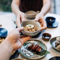 personal perspective of asian couple enjoying assorted dim sum and delicate dishes in chinese restaurant together. woman is serving a bowl of fried rice across the table to man. traditional chinese culture and food culture. y