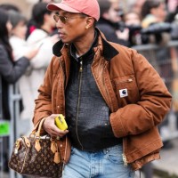 Pharrell Williams wears a light red cap, a brown oversized Sacai jacket, gold necklace, a black leather zipped jacket, a brown leather Louis Vuitton...