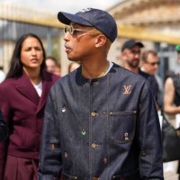 Pharrell Williams wears a navy blue denim with large white embroidered pattern cap, silver and gold rhinestones small circle sunglasses from Louis...