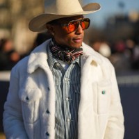 Pharrell Williams wears sunglasses , a white cowboy hat, a scarf, a black and white striped shirt, a white fluffy coat, outside Dior, during the...