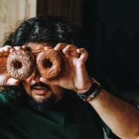 photo of young male student playfully holding two glazed doughnuts in front of eyes - junk food stock pictures, royalty-free photos & images