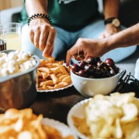 picture of hands of unrecognizable young people sitting on couch reaching for plates with yummy snacks - junk food stock pictures, royalty-free photos & images