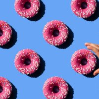 pink doughnut on pastel blue background. child's hand holding a donut. - junk food stock pictures, royalty-free photos & images