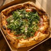 pizza with prosciutto and arugula leaves in box on table at home in bright sunlight. take-out comfort food concept. - junk food stock pictures, royalty-free photos & images