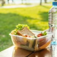 plastic container with sandwich, vegetables and fruits and a bottle of water on a table in a park in sunset - junk food stock pictures, royalty-free photos & images