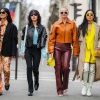 Pornwika Spiecker wears black sunglasses, silver earrings, a yellow / orange / black tie and dye print pattern shirt, matching yellow / orange /...