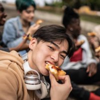 porträt eines jungen mannes, der mit freunden im park pizza isst - junk food stock-fotos und bilder