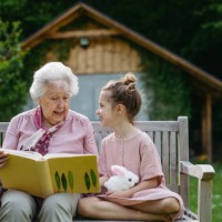 portrait granddaughter with grandmother, sitting on bench in the garden, reading book together. young girl enjoying together time with elderly grandma, looking at photos from photo album. - garden decoration photos et images 