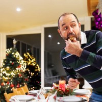 portrait of a man in casual clothes standing making a prank eating a sweet hidden looking away at christmas dinner, front view - food stock pictures, royalty-free photos & images
