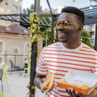 portrait of a young african-american man is eating hot dog and smiling - junk food stock pictures, royalty-free photos & images