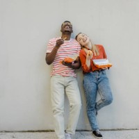 portrait of a young couple in front of the wall eating hot dog and smiling - junk food stock pictures, royalty-free photos & images