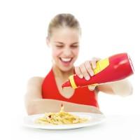 portrait of a young girl pouring ketchup onto a plate of french fries - junk food stockfoto's en -beelden