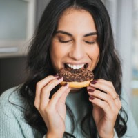 portrait of a young woman eating a donut in the kitchen - junk food stock pictures, royalty-free photos & images