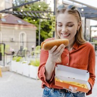 portrait of a young woman eating hot dog and smiling - junk food stock pictures, royalty-free photos & images