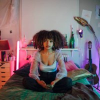 portrait of afro woman sitting with cross-legged on bed in illuminated bedroom at home - home decoration stock pictures, royalty-free photos & images