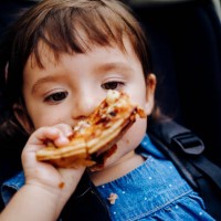 portrait of baby girl in stroller eating pizza - junk food stock pictures, royalty-free photos & images