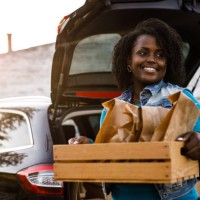 portrait of confident delivery woman holding a wooden crate with packages and order, looking away, smiling and contemplating - junk food stock pictures, royalty-free photos & images