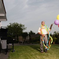 portrait of elderly man wearing birthday hat and streamers and holding balloons - garden decoration stock pictures, royalty-free photos & images