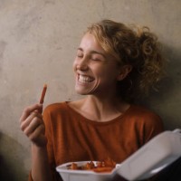 portrait of grinning young woman eating french fries at home - junk food stock pictures, royalty-free photos & images