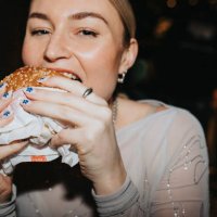 portrait of hungry woman taking bite of burger at bar - junk food stock pictures, royalty-free photos & images
