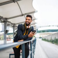 portrait of man commuter at the bus station using smartphone and waiting for bus. - travel stock-fotos und bilder
