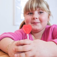 portrait of overweight girl holding heart shape lollipop - junk food stockfoto's en -beelden