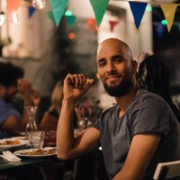 portrait of smiling young man with shaved head sitting at table during dinner party in backyard - garden decoration stock pictures, royalty-free photos & images