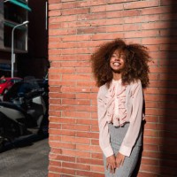 portrait of smiling young woman with afro hairdo leaning against brick wall in the city - fashion stock pictures, royalty-free photos & images