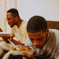 portrait of two men eating takeout food on sofa at home,tema,ghana - junk food stock pictures, royalty-free photos & images