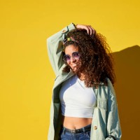 portrait of woman with sunglasses touching her afro hair on yellow background - fashion stock pictures, royalty-free photos & images