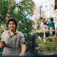 portrait of young man holding mobile phone while standing in backyard - garden decoration stock pictures, royalty-free photos & images