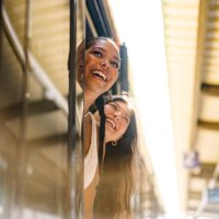 portrait shot of two young women looking out of an open door of a train on a platform and smiling - travel stock pictures, royalty-free photos & images