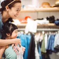 pretty young mom trying on clothes with her lovely little daughter in a fashion boutique joyfully. - fashion photos et images de collection
