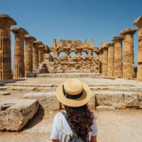 rückansicht einer frau mit hut, während sie einen antiken tempel in sizilien bewundert - travel stock-fotos und bilder