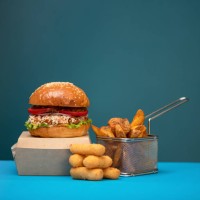 ready-to-eat takeaway food. cardboard box with fresh hamburger, fried potatoes and chicken nuggets or croquettes on blue background. fast food restaurant menu. side view. copy space at top of image - junk food stock pictures,