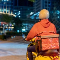 rear-view of delivery person driving scooter through city in the night - food stock pictures, royalty-free photos & images