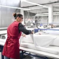 rear view of expert female textile worker unrolling material rolls for cutting - fashion stock pictures, royalty-free photos & images