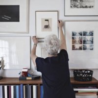 rear view of retired senior woman adjusting picture frame on wall over bookshelf at home - home decoration stock pictures, royalty-free photos & images