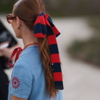 Rebecca Ferraz-Wyatt is seen wearing a blue and red striped bow in her hair; oversize round sunglasses with Havana frame and orange gradient lenses...